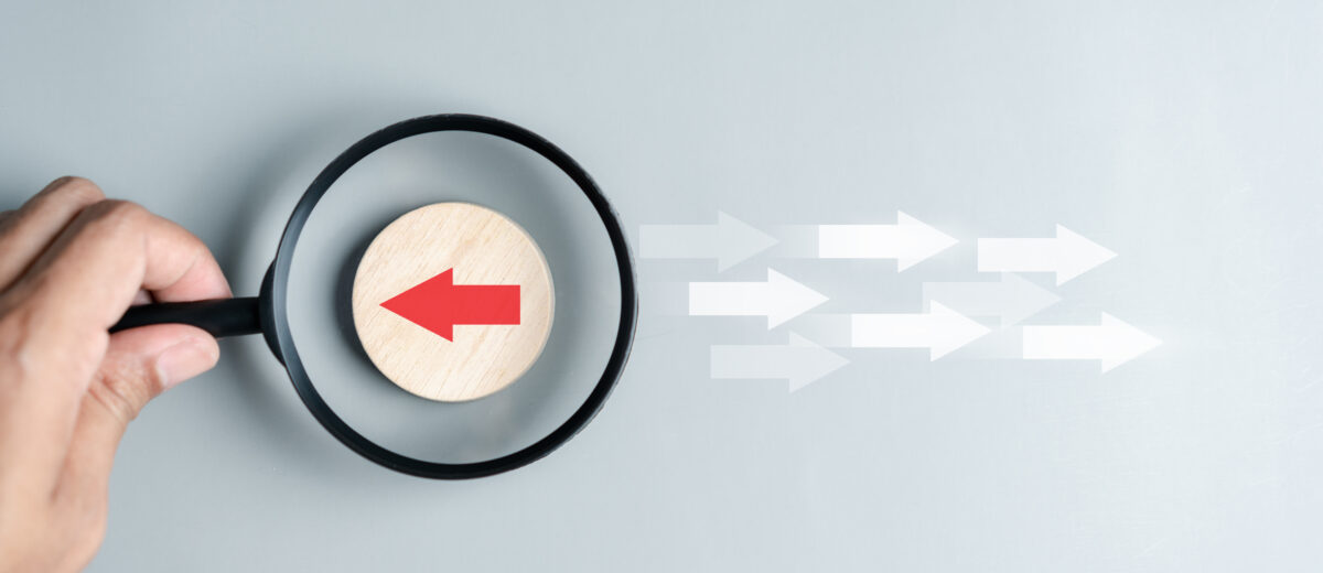 Hand holding magnifier focus to Red arrow and different direction facing opposite direction with white arrow for business disruption and technology transformation and different thinking idea concept.