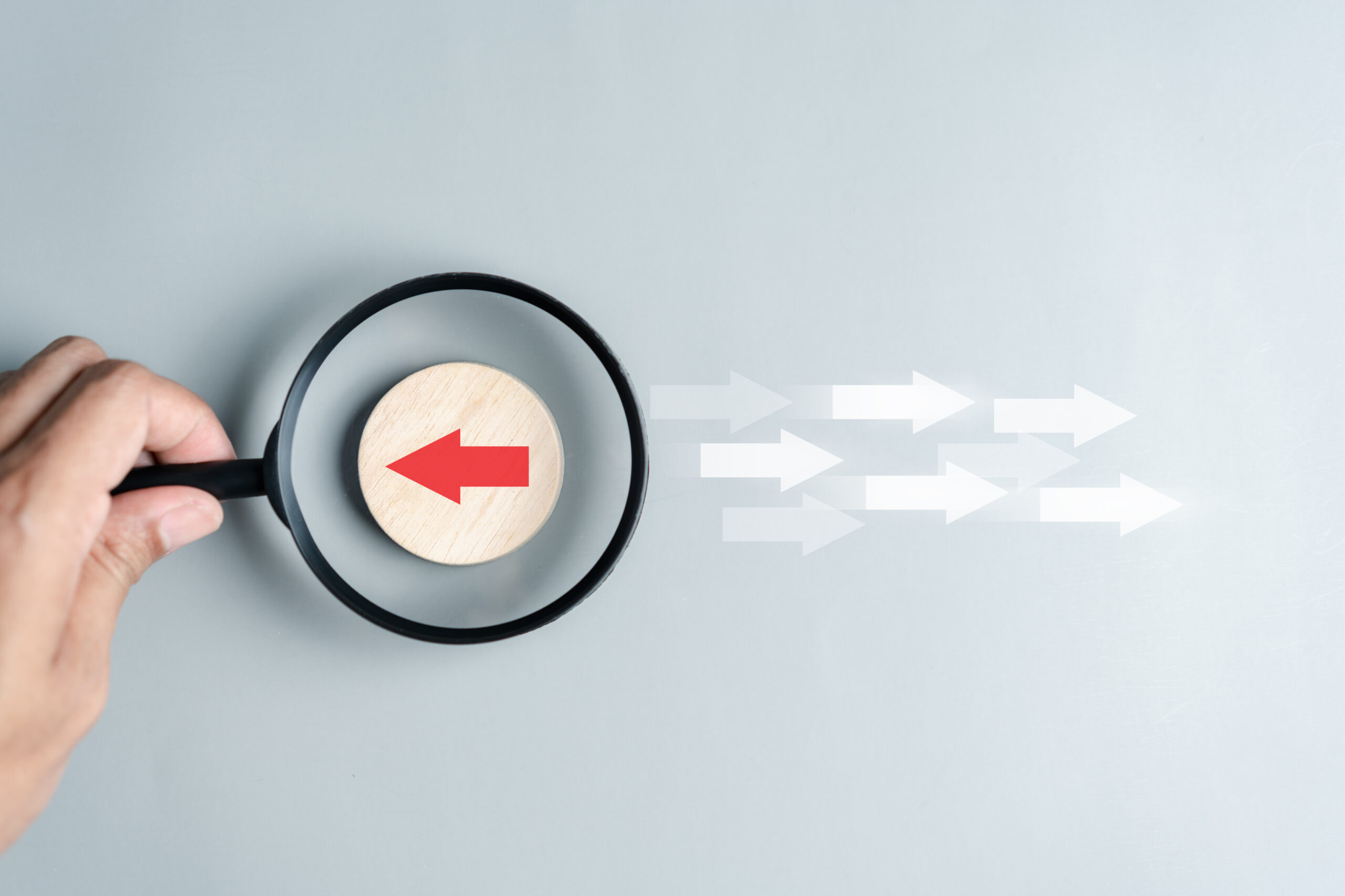 Hand holding magnifier focus to Red arrow and different direction facing opposite direction with white arrow for business disruption and technology transformation and different thinking idea concept.
